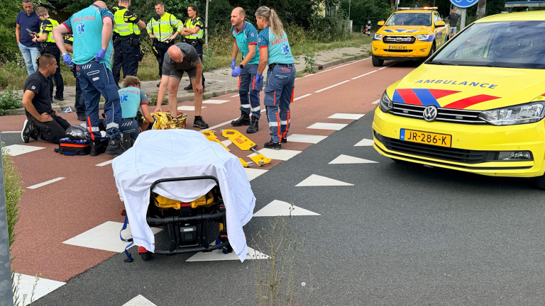 Hulpverleners en politie verlenen eerste hulp op de weg naast een ambulance en brancard met laken