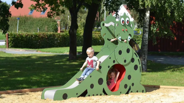 Kinderen spelen op een groene krokodilvormige glijbaan in een zandbak in het park