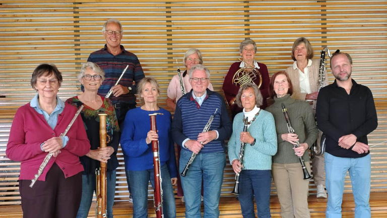 Groepsfoto van muzikanten met fluiten, fagotten, hobo, hoorn en basklarinet voor een houten wand
