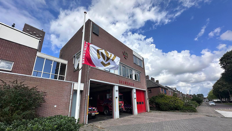 Brandweerkazerne met rode garagedeuren en een vlag met tekst “BRANDWEER” aan de vlaggenmast