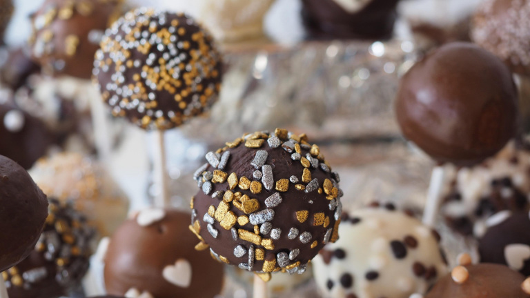Chocolade cake pops met goud- en zilverkleurige sprinkles, met andere cake pops onscherp op de achtergrond