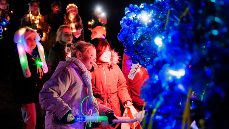 Kinderen en volwassenen bewonderen ’s avonds een felblauwe lichtinstallatie tijdens een feestelijk lichtfestival