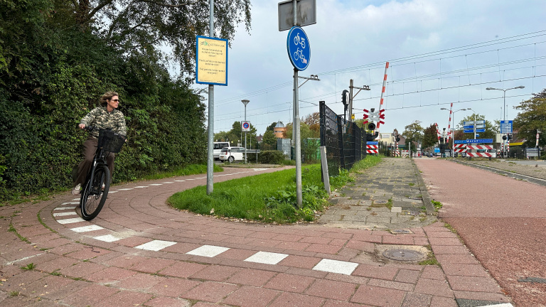 Fietser op rood fietspad langs een spoorwegovergang met slagbomen en borden, bij station Castricum