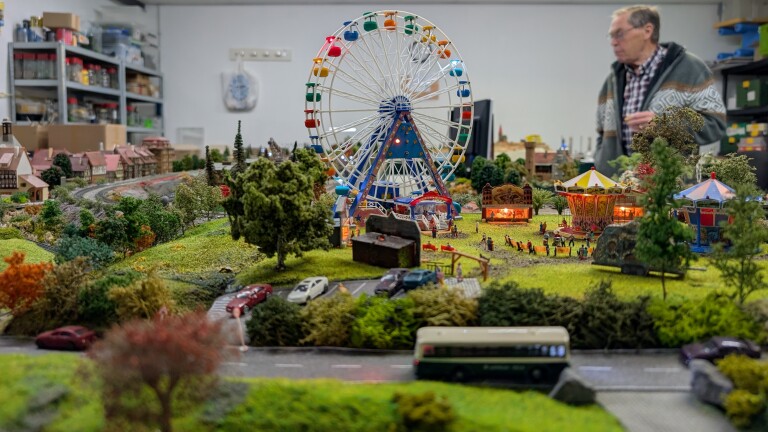 Miniatuurkermis met reuzenrad en draaimolen in modeldorp, met autootjes en een man op de achtergrond
