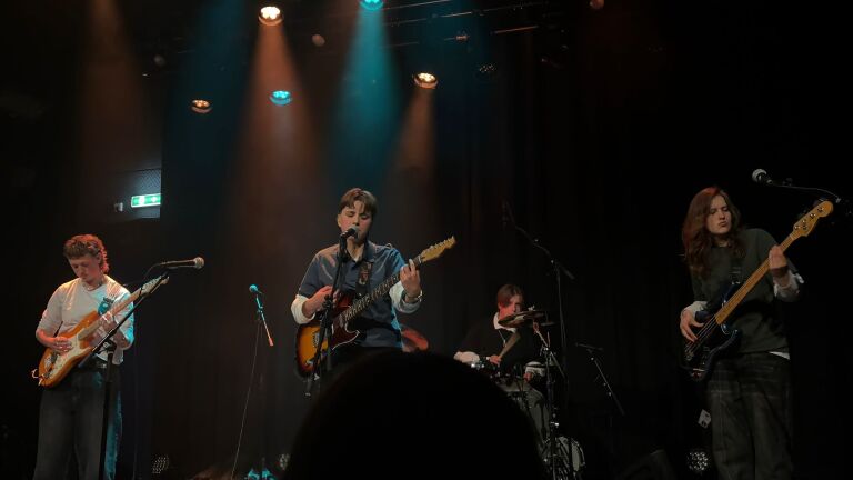Band op podium met zanger-gitarist, tweede gitarist, drummer en bassist onder gekleurde spotlights