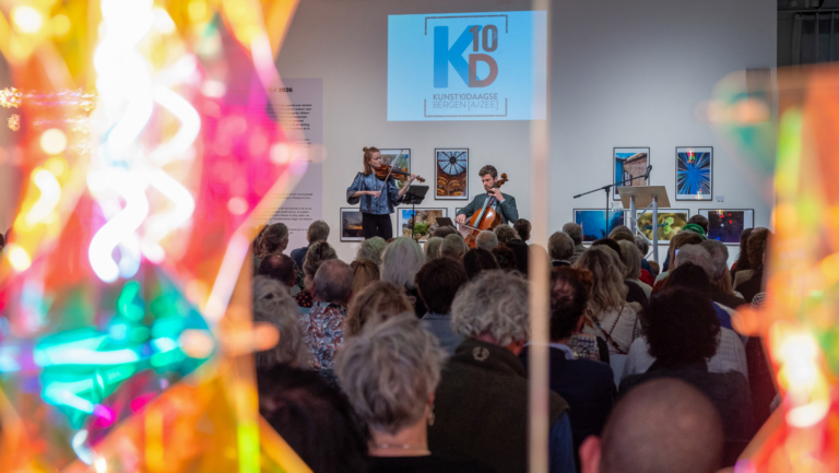 Publiek luistert naar viool- en celloconcert in galerie, met projectie “Kunst10Daagse Bergen (A/ZEE)” op de muur