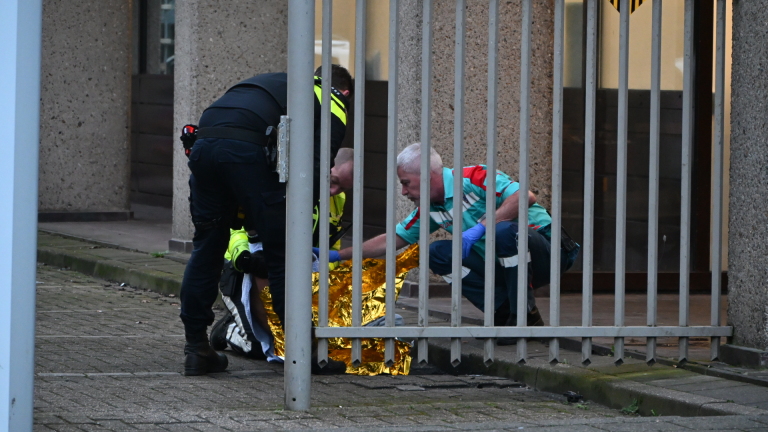 Politieagent en medische hulpverlener zorgen voor een persoon die op de grond ligt, waarbij ze een reddingsdeken gebruiken.
