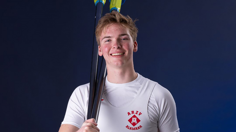 Lachende roeier in wit shirt met ARZV Alkmaar-logo, met roeiriem over de schouder tegen donkerblauwe achtergrond