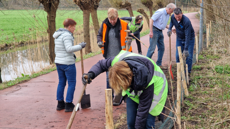 Personen werken samen buiten op een pad, bezig met het plaatsen van houten palen langs de rand.