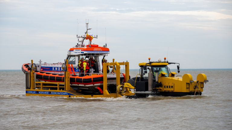 Reddingsboot op water met KNRM-insignia samen met een gele sleeptractor, bemand door reddingspersoneel.