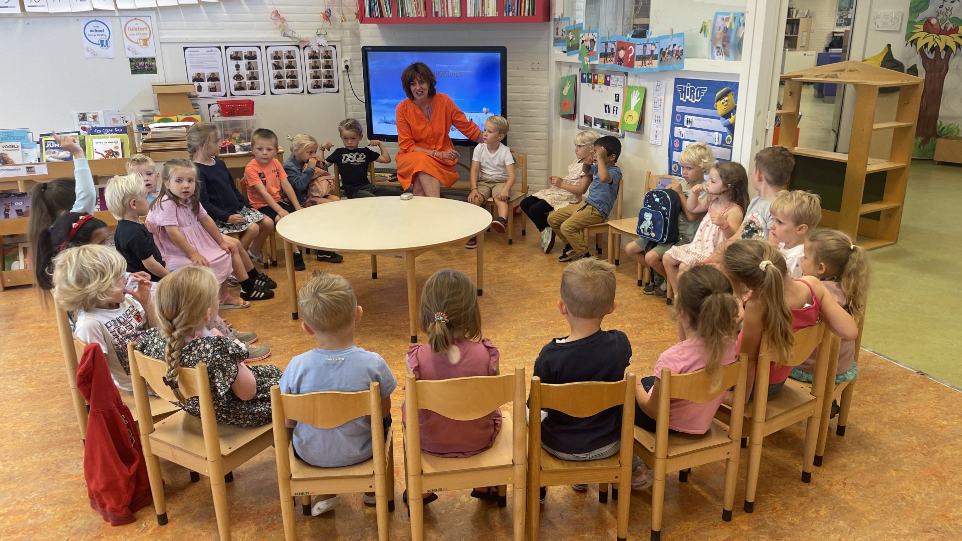 De kleuters van basisschool de Klimduin zitten in een kring in een klaslokaal met juf Deet.