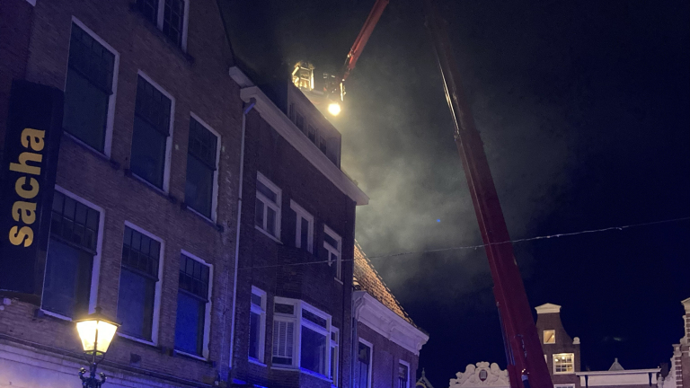 Brandweer op het dak van een gebouw, bezig met het blussen van een brand in de nacht.