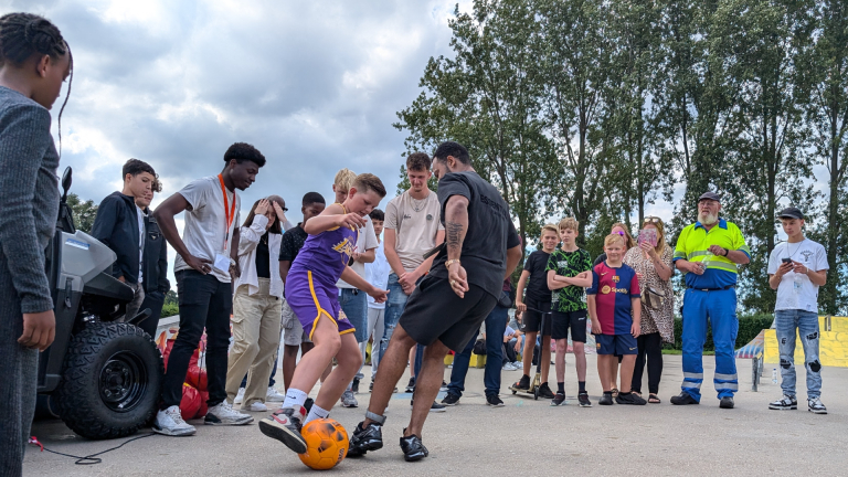 Jonge mensen kijken toe terwijl een man en een jongen voetballen op straat.