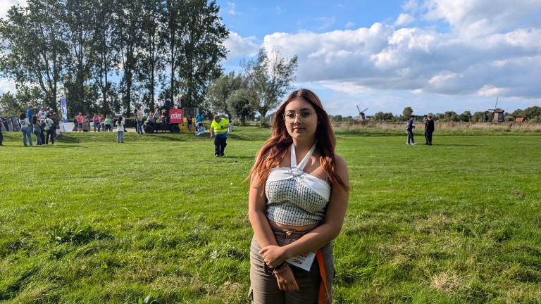 Een vrouw staat op een grasveld met mensen en molens op de achtergrond.