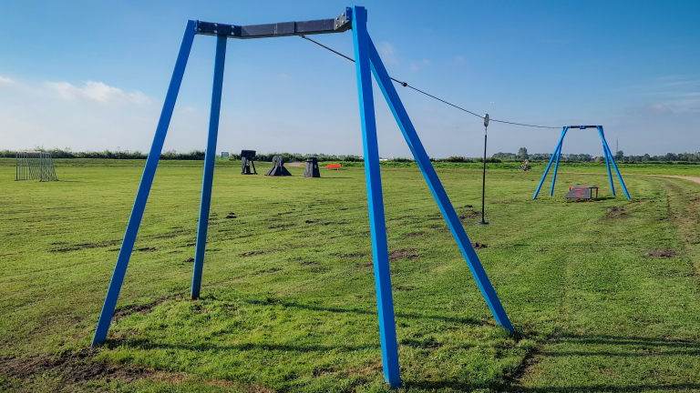 Blauw stalen frame van een kabelbaan op een grasveld onder een heldere blauwe hemel.