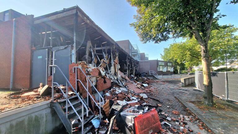 Verwoest en verbrand gebouw met ingestorte muren, puin op de grond en een beschadigde gevel.