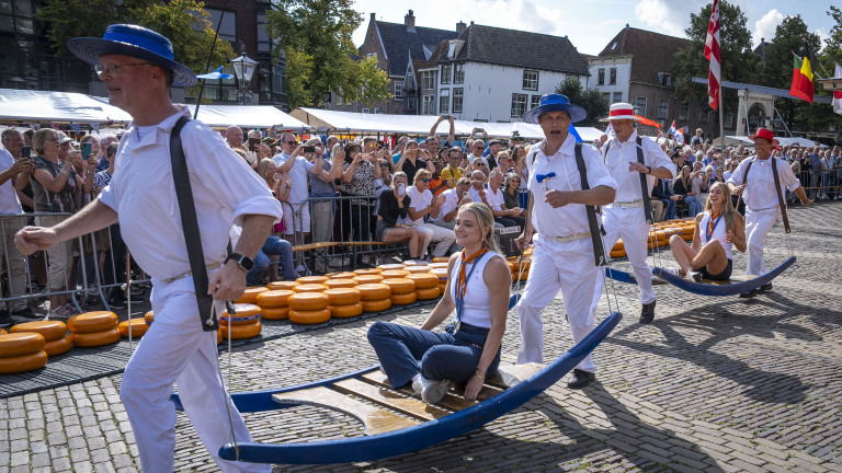 De kaaskragers van Alkmaar dragen toeristen op traditionele kaasberries tijdens de kaasmarkt, met een menigte toeschouwers op de achtergrond.