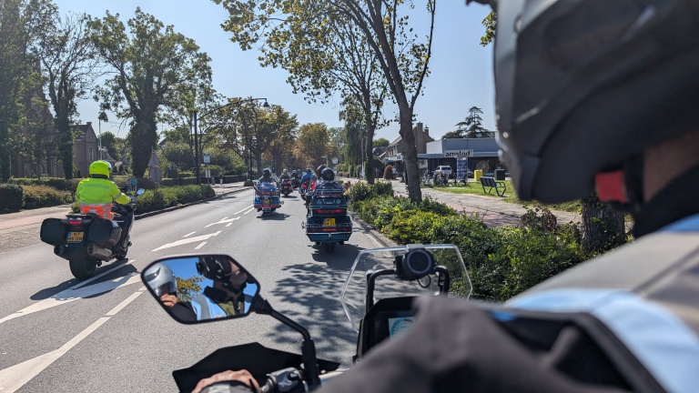 Groep motorrijders onderweg op een zonnige dag, met de voorste motorrijder in een felgele jas.