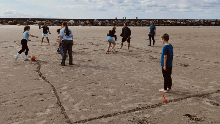 Mensen spelen een balspel op het strand met een getekend veld in het zand.