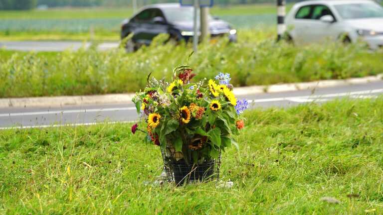 Boeket bloemen in een mand op een groene wegberm, met auto's op de achtergrond.