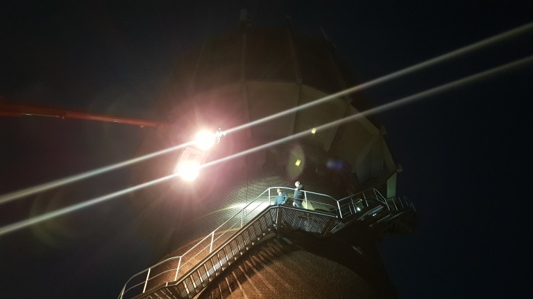 Mensen die 's nachts een trap op een hoog gebouw beklimmen met felle verlichting erboven.