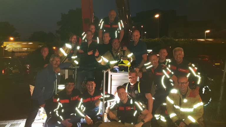 Groepsfoto van vrijwilligers van de brandweer in uniform, buiten bij avond.