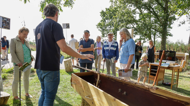 Groep mensen kijkt naar een houten boot op een buitententoonstelling.