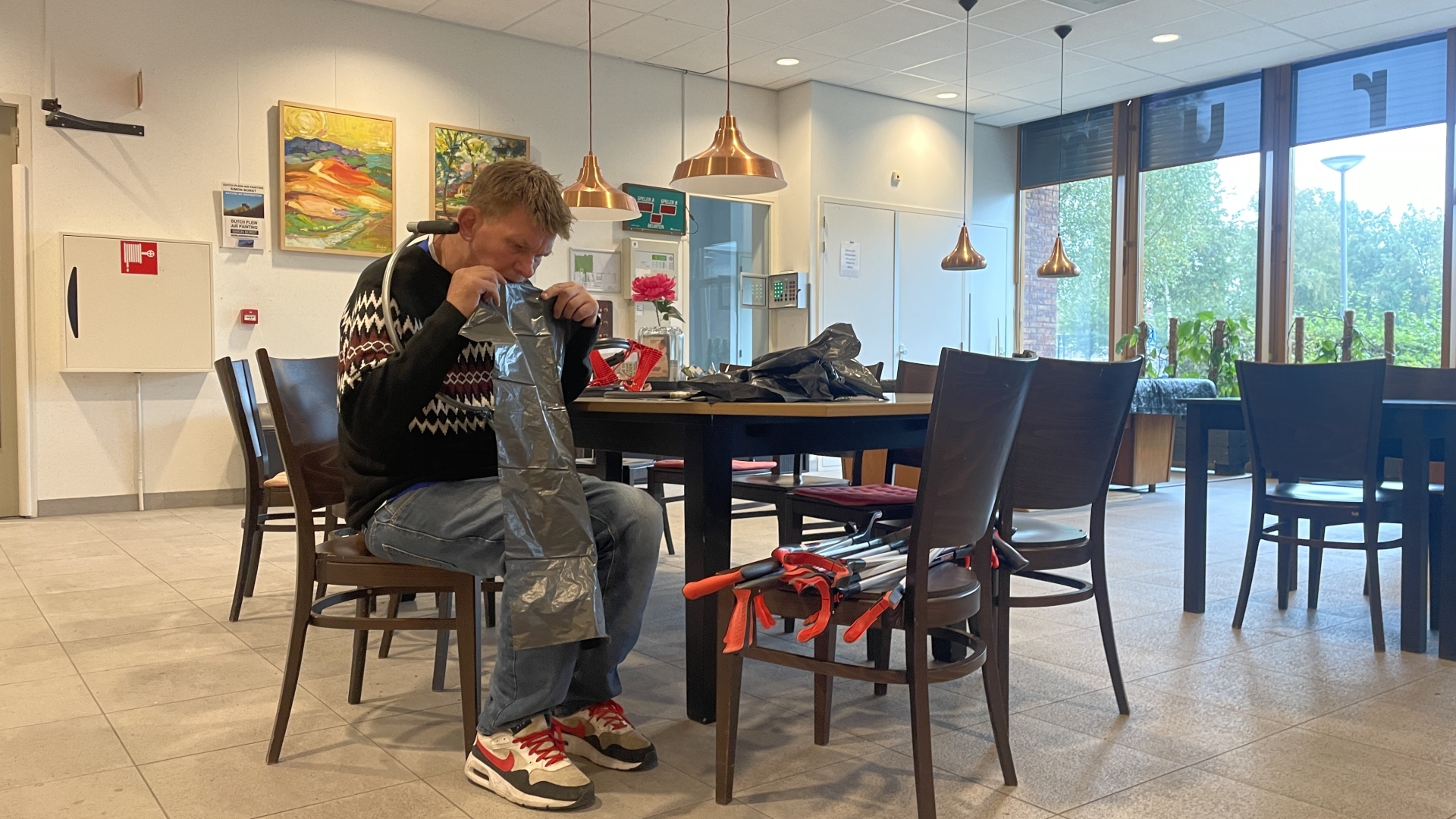 Man in een restaurant die een vuilniszak openmaakt, zittend aan tafel met schoonmaakgereedschap om hem heen.