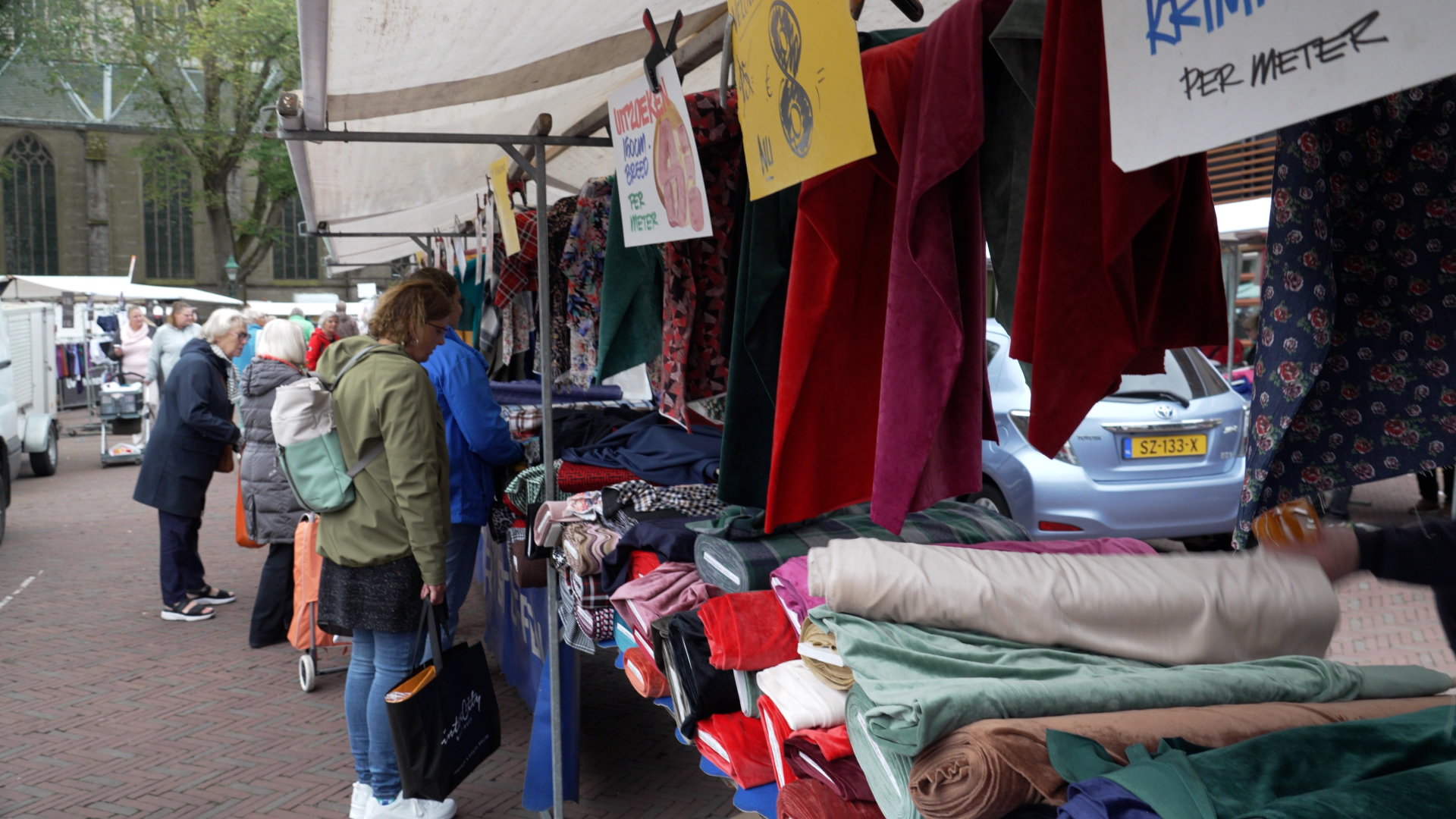 Marktkraam met stoffen en bezoekers op een markt.