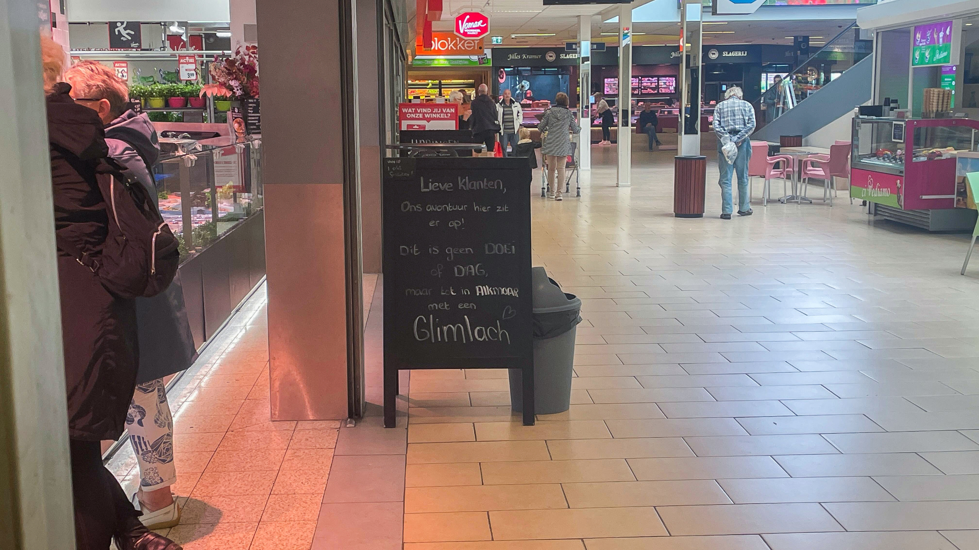 Gangpad van een winkelcentrum met een zwart bord waarop een afscheidsboodschap staat.