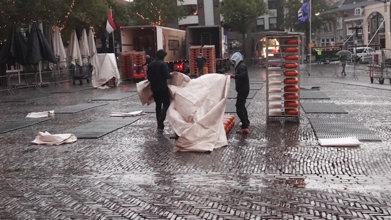 Mensen zetten een markt op in de regen, met plastic hoezen en rekken vol ronde kaas.