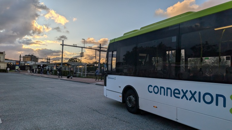 Connexxion bus bij een OV-station tijdens zonsondergang met mensen op de achtergrond.