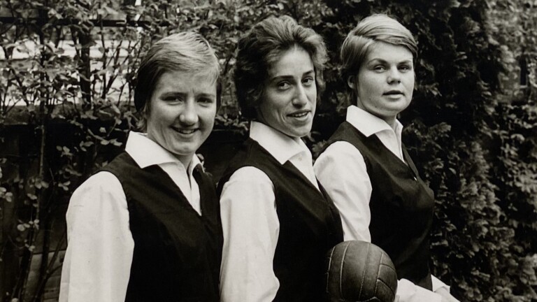 Drie vrouwen in uniformen met een voetbal, buiten gefotografeerd in zwart-wit.