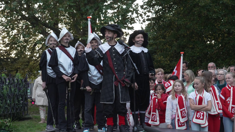 Groep kinderen in historische kostuums voert een act op voor toeschouwers in een park.