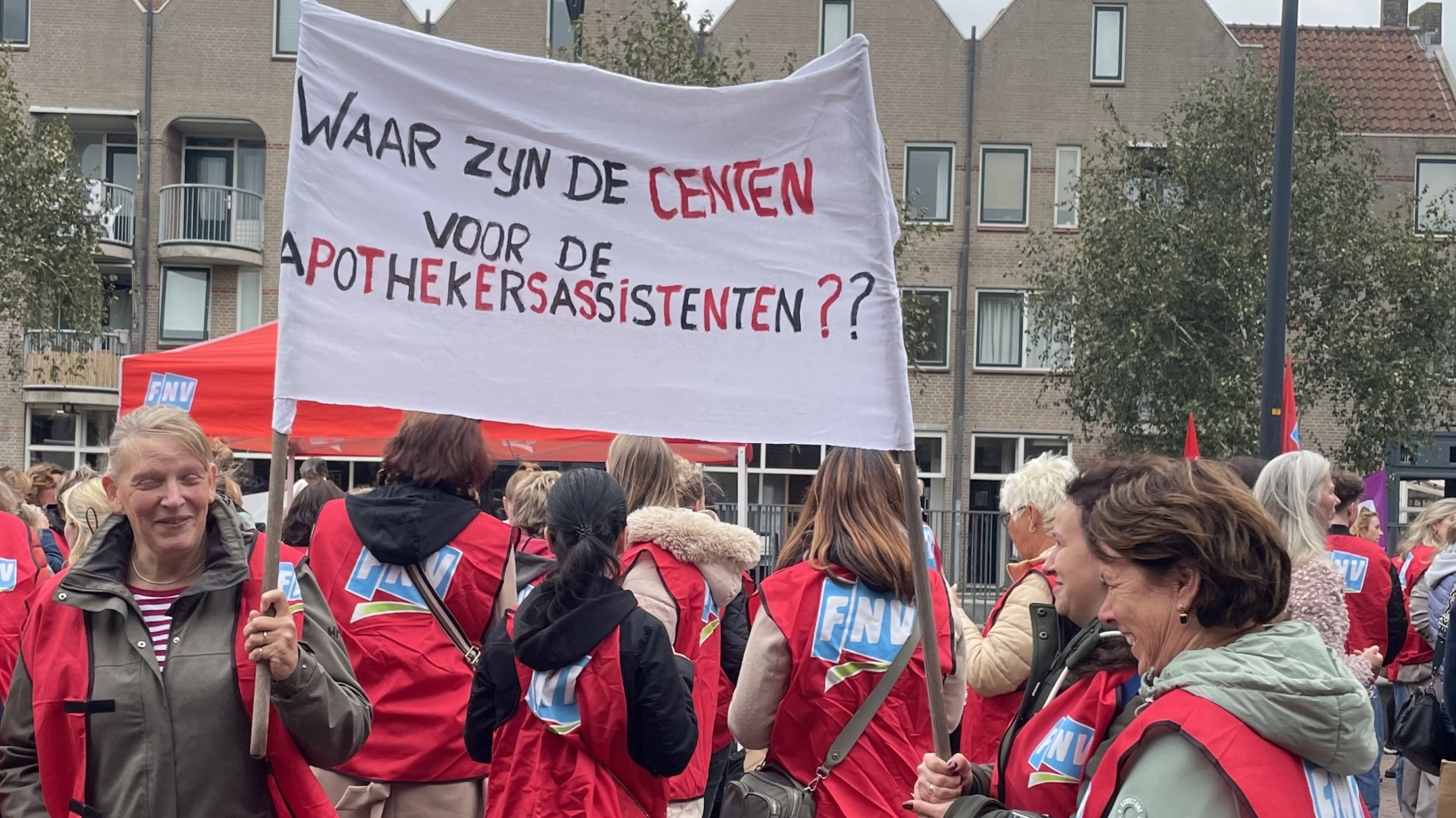 Een groep mensen met FNV-hesjes houdt een protestbord vast met de tekst "Waar zijn de centen voor de apothekersassistenten??".