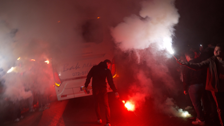 Mensen met fakkels en rook rond een bus 's nachts.