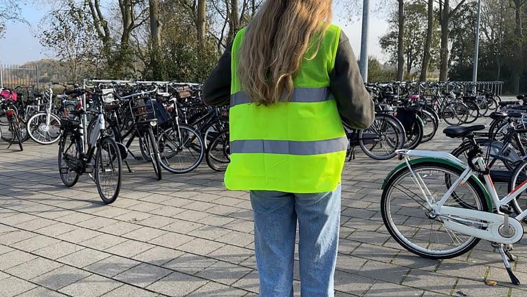 Persoon in een geel veiligheidshesje bij een fietsenstalling.