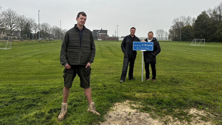 Drie mannen op een grasveld naast een bord met de tekst "Buurschap 't Kruis gem. Dijk en Waard".