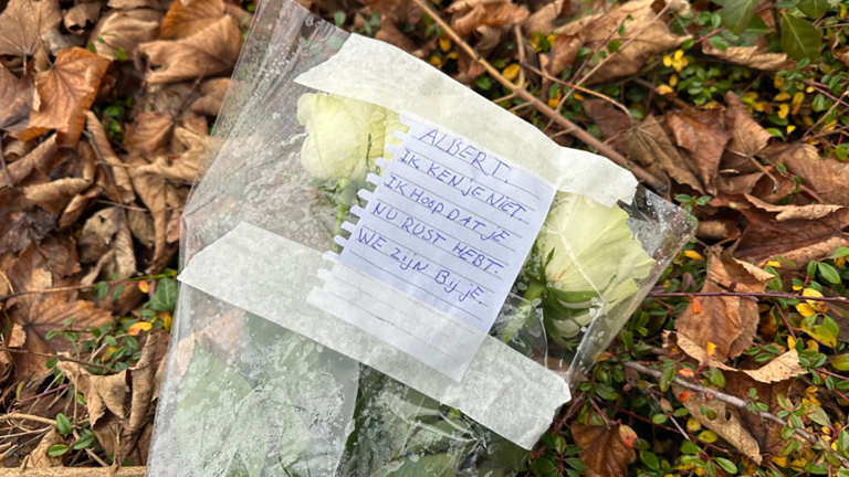 Een boeket witte rozen op de grond, omwikkeld met cellofaan en vergezeld van een handgeschreven briefje.