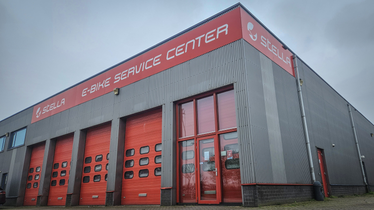 Grijs gebouw met rode garagedeuren, met opschrift "STELLA E-BIKE SERVICE CENTER".