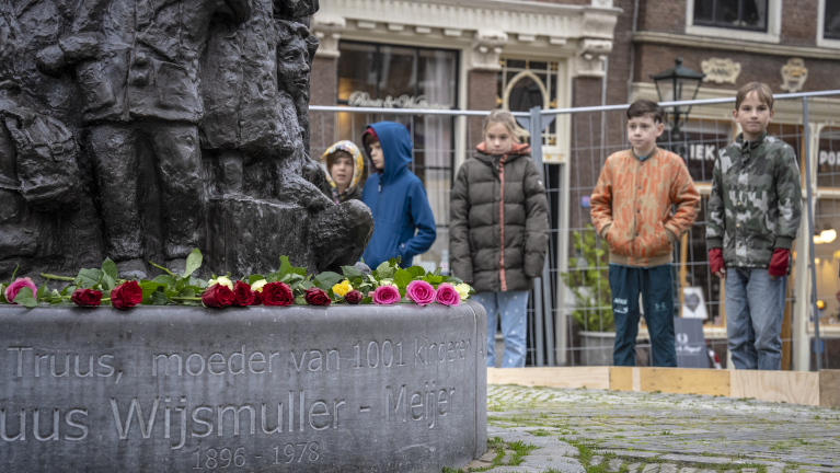 Kinderen staan voor een monument met rozen erop, met inscriptie "Truus Wijsman-Meijer."