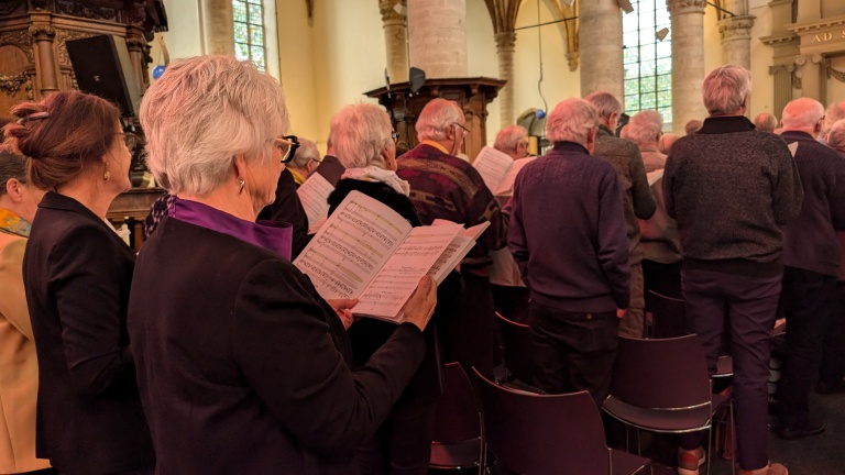 Mensen staan in de kerk en zingen uit bladmuziek.