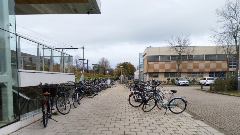 Fietsenstalling met veel geparkeerde fietsen naast een gebouw op een bewolkte dag.