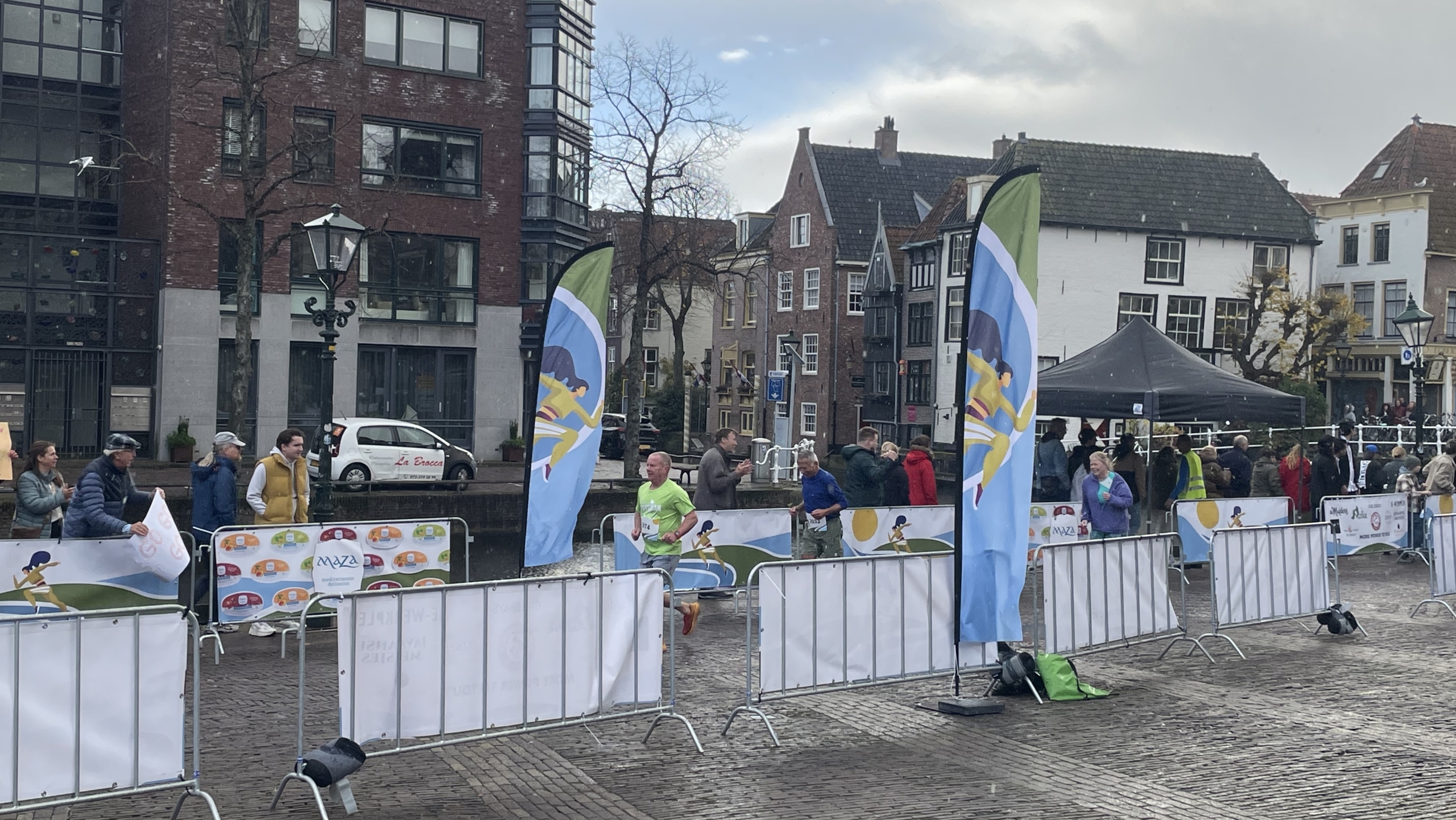 Loopwedstrijd met toeschouwers en vlaggen in een stadsomgeving met historische gebouwen.