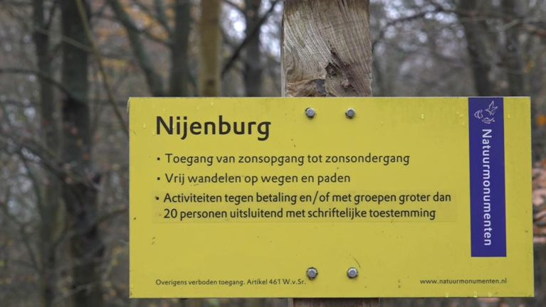 Geel bord met tekst over toegang tot Nijenburg en regels voor activiteiten, geplaatst in een bosomgeving.