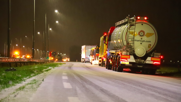 Vrachtwagens rijden 's nachts over een besneeuwde snelweg.