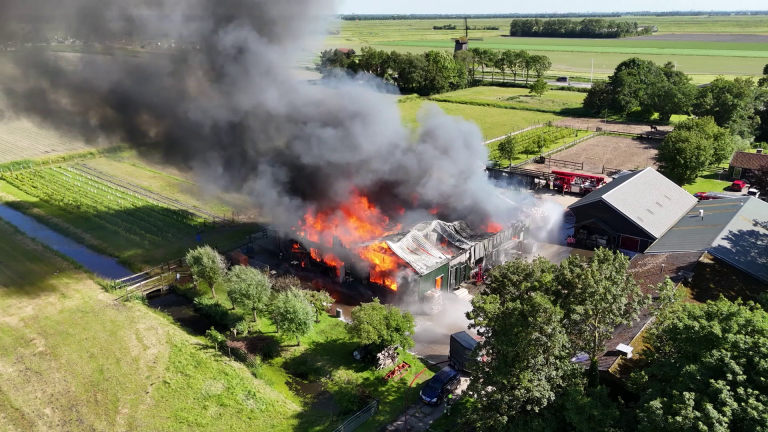 Brandend gebouw op het platteland, met dikke zwarte rookwolken die opstijgen.