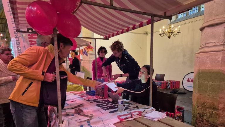 Mensen bij een marktkraam in gesprek, met ballonnen en informatiemateriaal op tafel.