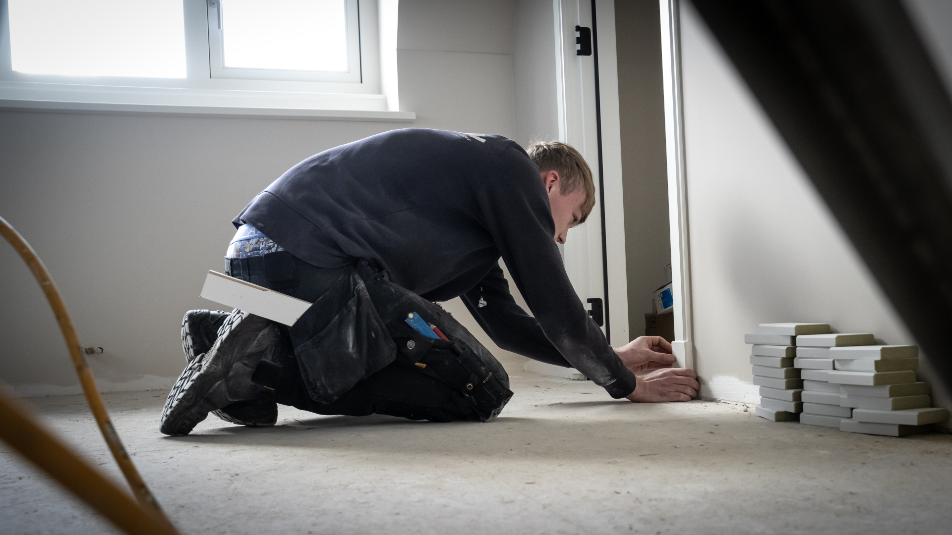 Man installeert plint in een kamer met gereedschap en stapel plinten dichtbij.