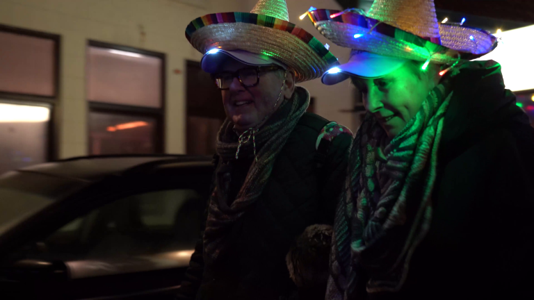 Twee mensen dragen hoeden met gekleurde verlichting op straat.